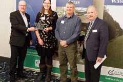 Pat Brown, Vivian Crump, Chris Crump and Mike Stark stand in front of St. Clair Region Conservation Authority banners with Pat and Vivian holding a glass award