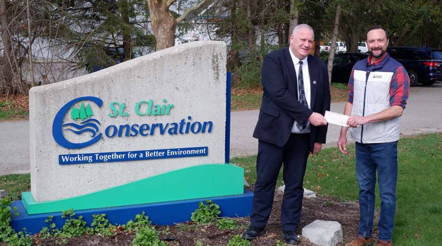 Two men standing beside a St. Clair Region Conservation Authority sign holding a cheque