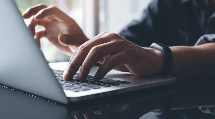 Two hands typing on the keyboard of a laptop