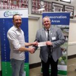 Two men shaking hands holding a cheque