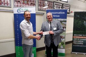 Two men shaking hands holding a cheque