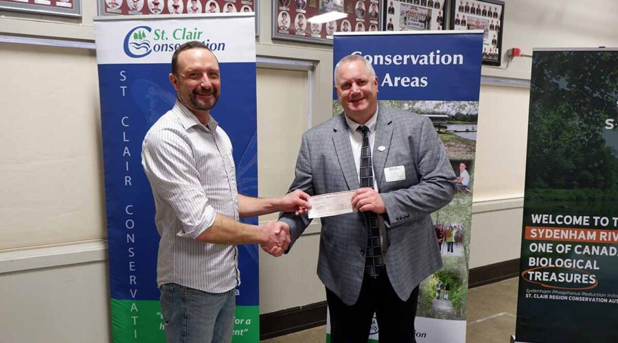 Two men shaking hands holding a cheque