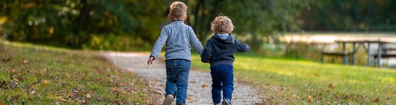 2 children holding hands waling on a forest trail