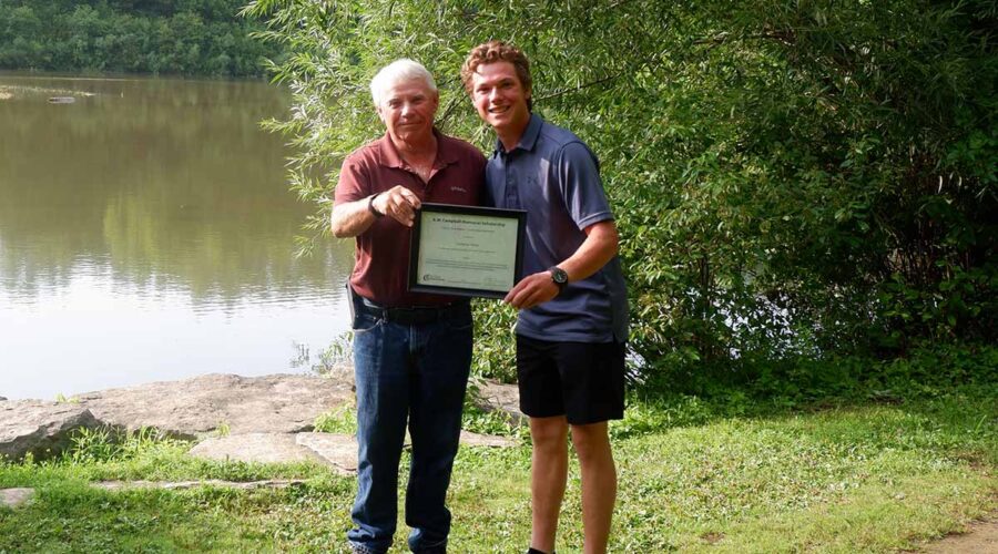 Two people stand in front of a reservoir holding a certificate.