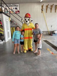 A dog mascot wearing a fire suit with four children